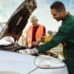 Two road assistant workers in towing service trying to start car engine with jump starter and energy station with air compressor. Roadside assistance concept.